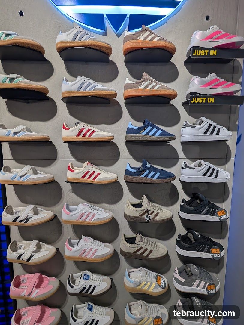 The exterior of a sports store with large illuminated signage that reads "SPORTS.MY". Below the sign, the store window displays various athletic shoes on shelves. A yellow grid pattern is visible behind the signage. The store appears to be located within a mall, as indicated by the ceiling and adjacent shop fronts.