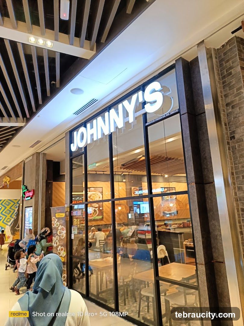 The exterior of a Johnny's restaurant with large glass windows and prominent signage. Inside, tables and chairs are visible, along with customers dining.