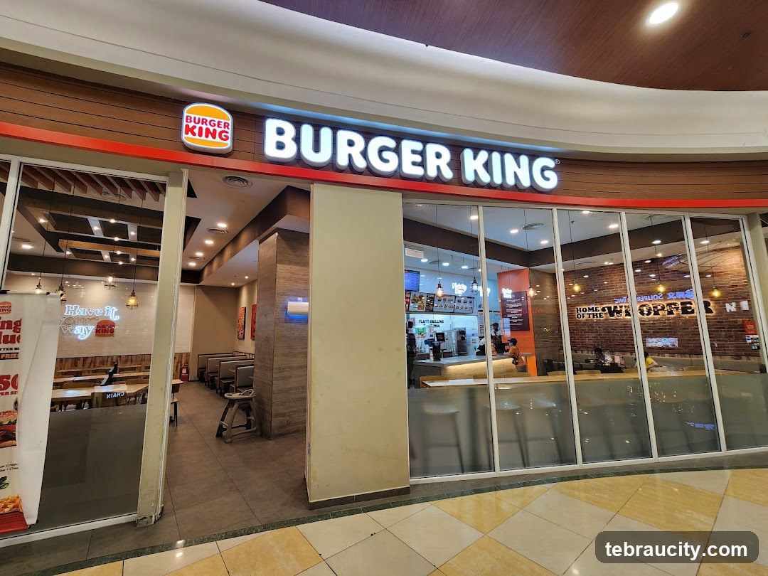 The exterior of a Burger King restaurant with its prominent signage visible. The entrance is open, revealing the interior seating area and counter.