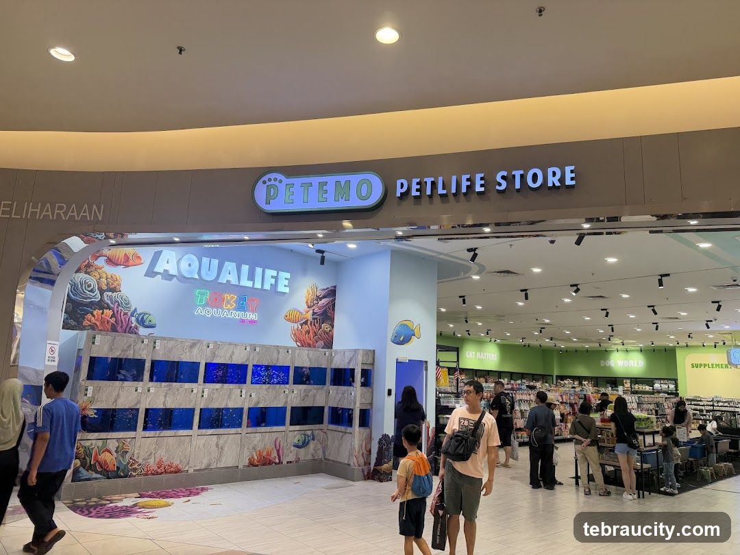 The exterior of a pet store with a prominent sign reading "PETEMO PETLIFE STORE". To the left, an entrance area displays "AQUALIFE TOKEY AQUARIUM" with rows of fish tanks. Inside, the store is visible with sections labeled "CAT MATTERS", "DOG WORLD", and "SUPPLEMENTS". Several customers are browsing the merchandise.