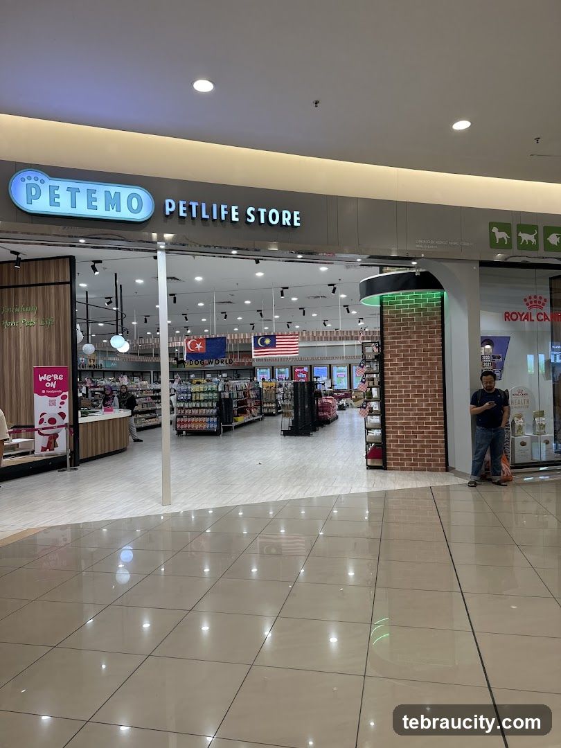 The exterior of a pet supply store called Petemo Petlife Store. The store has a wide entrance with shelves stocked with pet products visible inside. There are flags displayed near the entrance. A man is standing to the right of the entrance, looking at his phone.