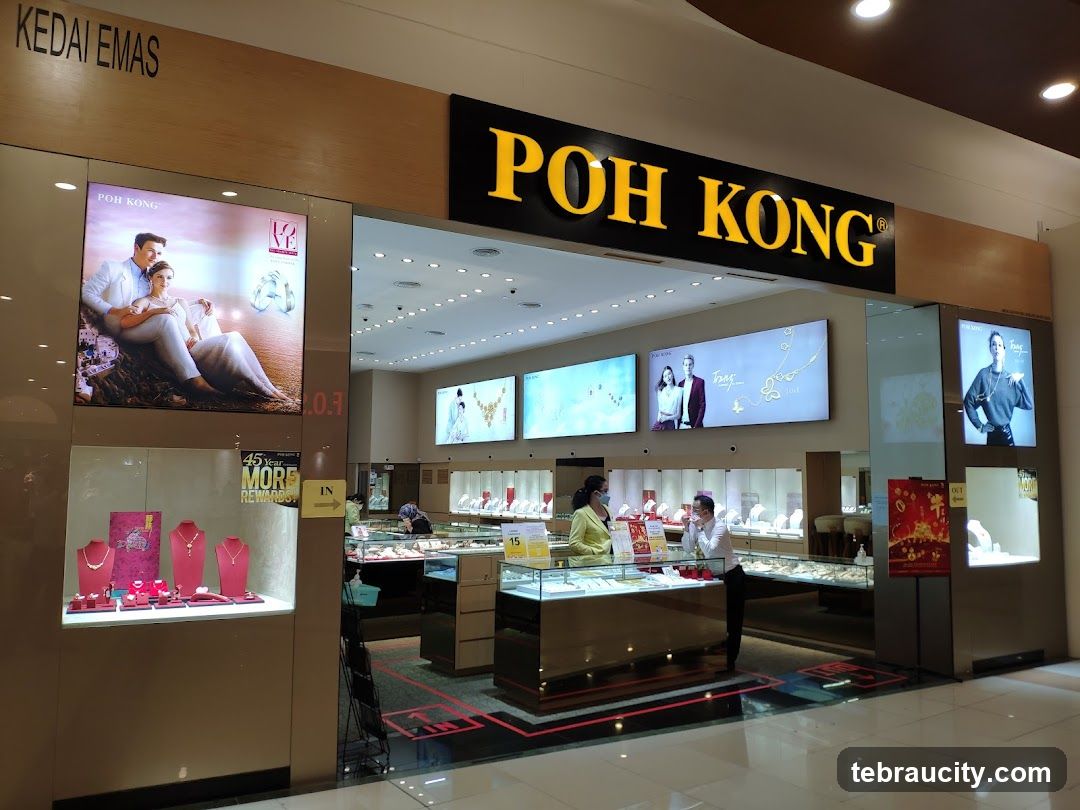 The exterior of a Poh Kong jewelry store. A large sign with the store name "POH KONG" is visible above the entrance. Display cases with jewelry are visible inside, and promotional images are displayed on screens.