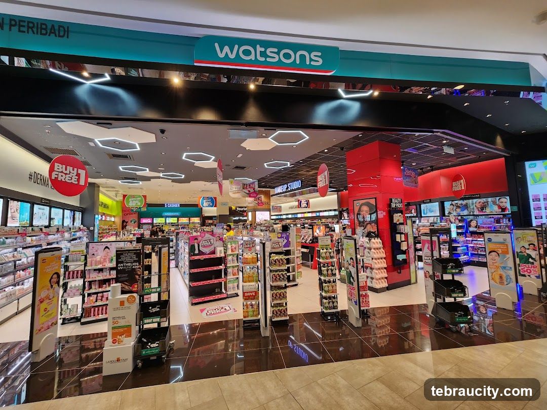 The exterior of a Watsons store, a health and beauty retailer, is shown. The store has a wide entrance with displays of various products visible inside. The Watsons logo is prominently displayed above the entrance. Promotional signs for "BUY 1 FREE 1" and "#DERMA" are also visible. The interior is brightly lit and stocked with a wide array of cosmetics, skincare, and personal care items.
