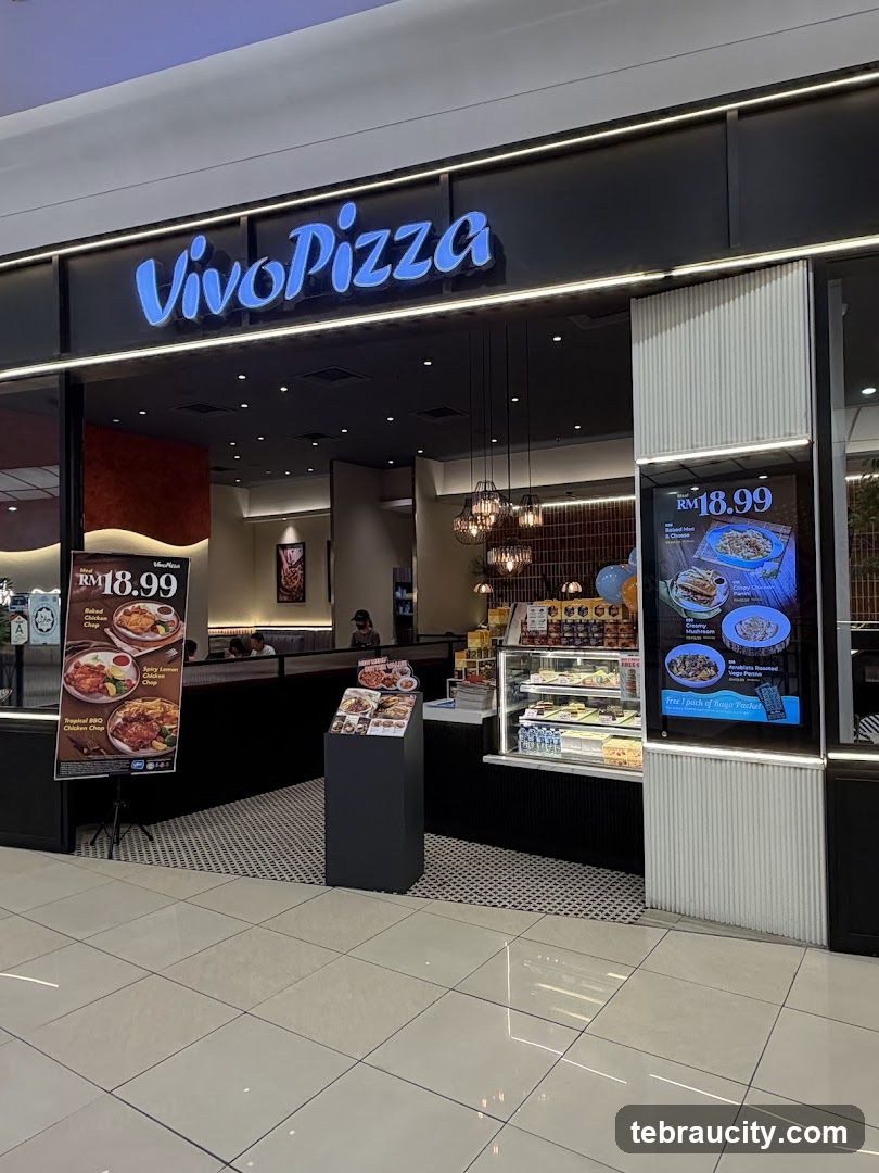 The exterior of a Vivo Pizza restaurant with a prominent blue neon sign above the entrance. To the left, a display board shows meal deals with prices and images of food. To the right, a digital screen displays menu items and promotions. The entrance area features a counter with a display case and seating visible inside.