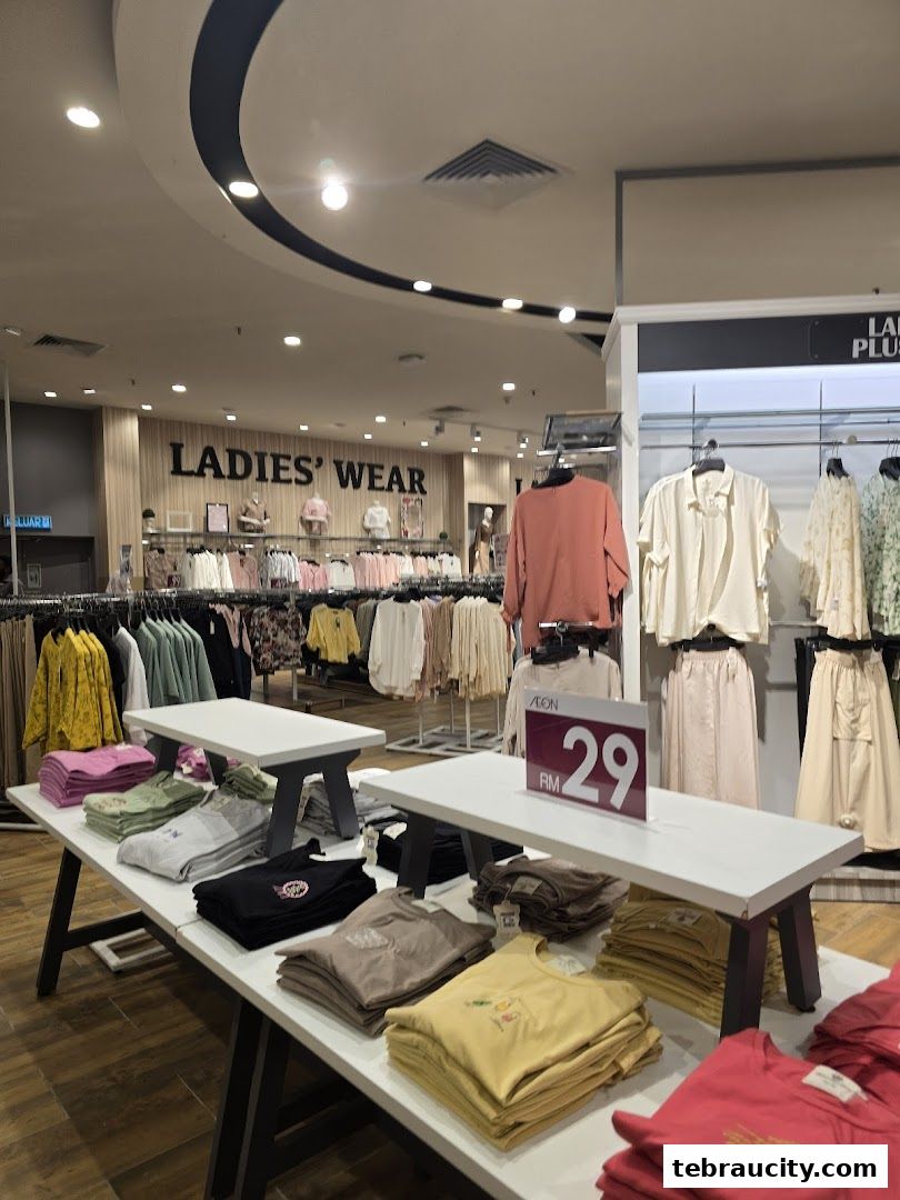 Interior view of a clothing store section dedicated to ladies' wear, featuring folded t-shirts and racks of apparel.