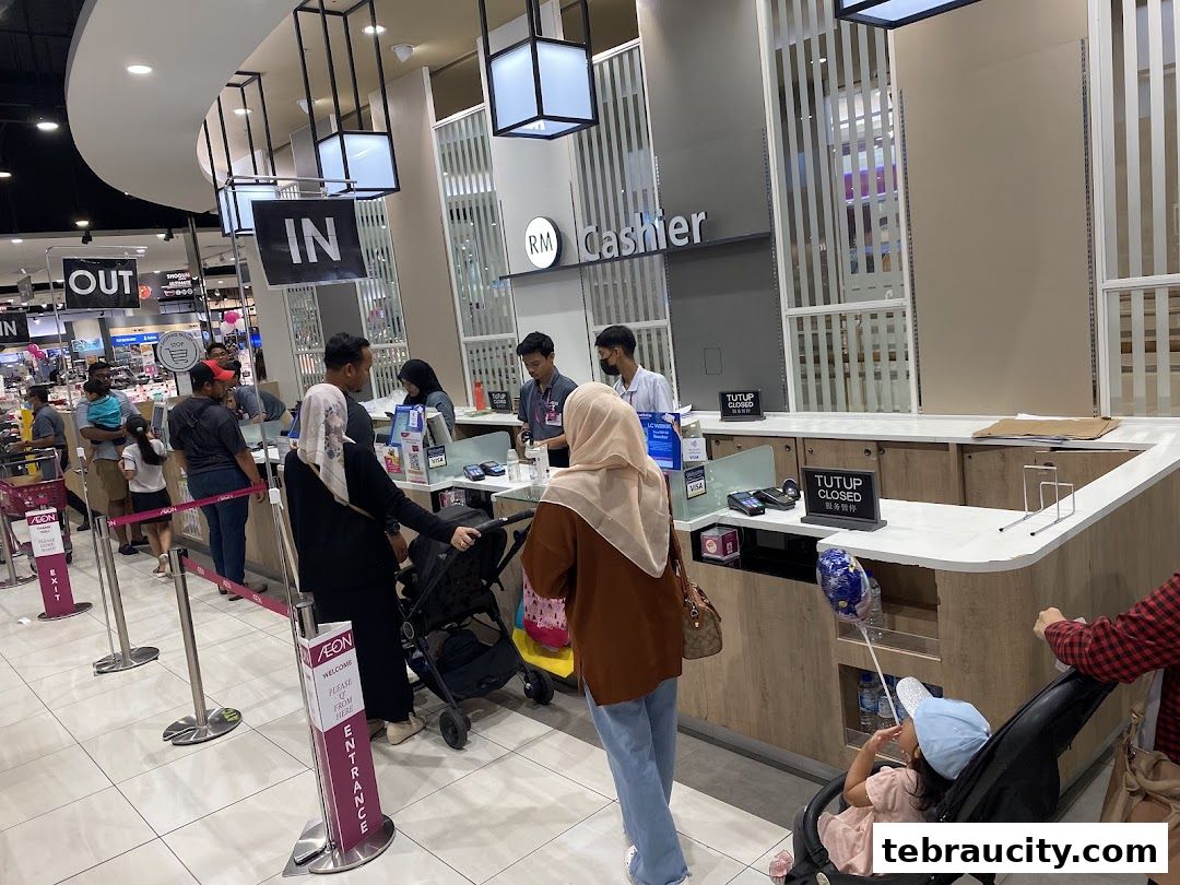 Customers queue at the cashier counter of AEON Tebrau City JB, with 'IN' and 'OUT' signs visible.