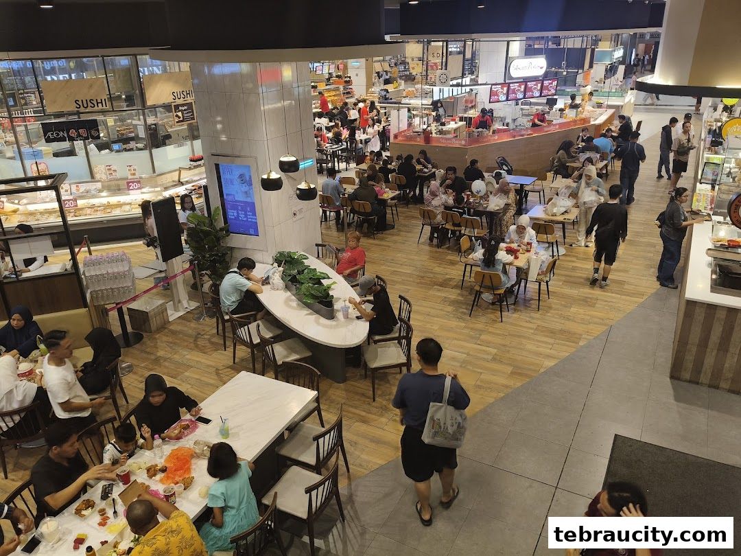 A busy food court with many people dining and queuing at various food stalls.