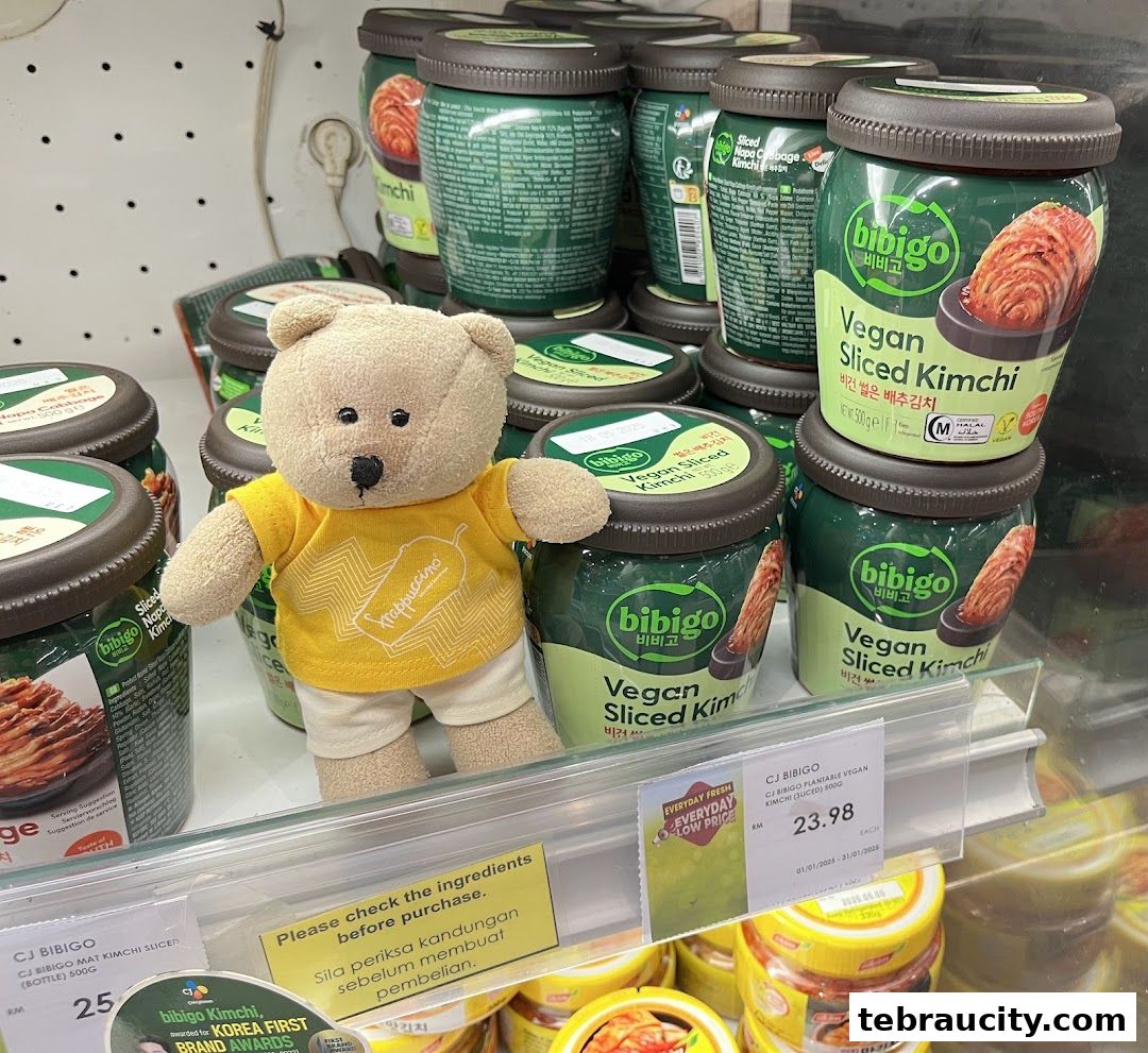 A teddy bear stands in front of shelves stocked with Bibigo Vegan Sliced Kimchi jars.