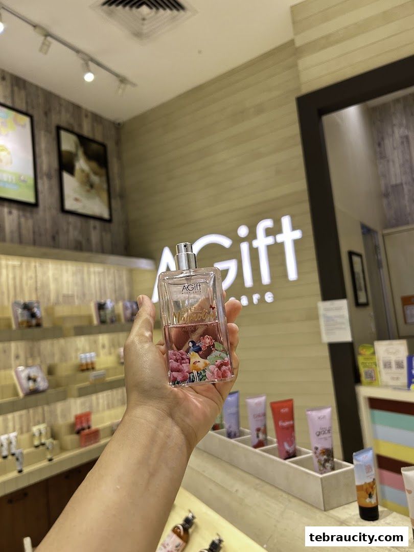 A hand holds a perfume bottle with floral designs in front of a shop interior.