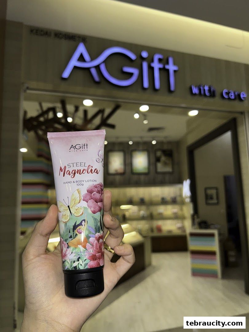 A hand holds a tube of hand and body lotion in front of the AGift shop.