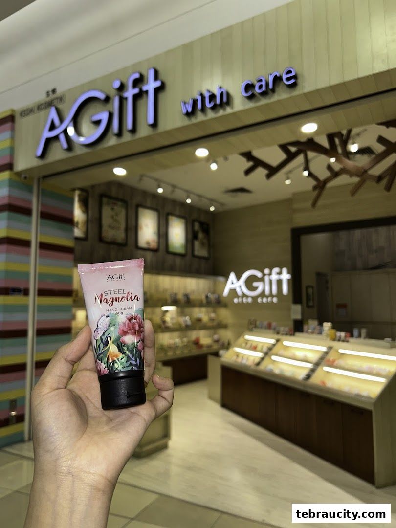 A hand holds a tube of hand cream in front of a brightly lit cosmetics shop.