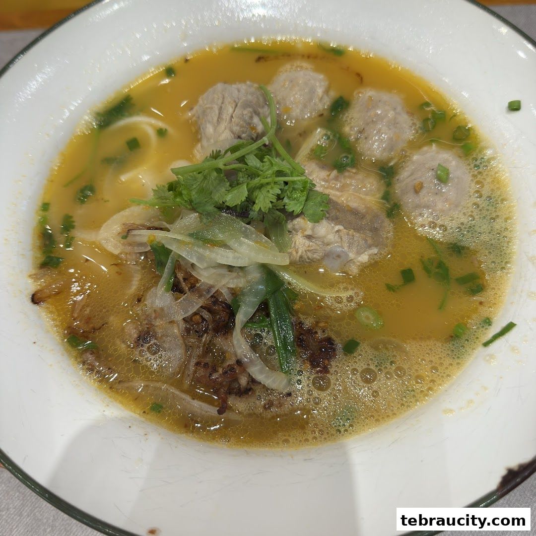 A close-up shot of a steaming bowl of Vietnamese noodle soup with meatballs and herbs.