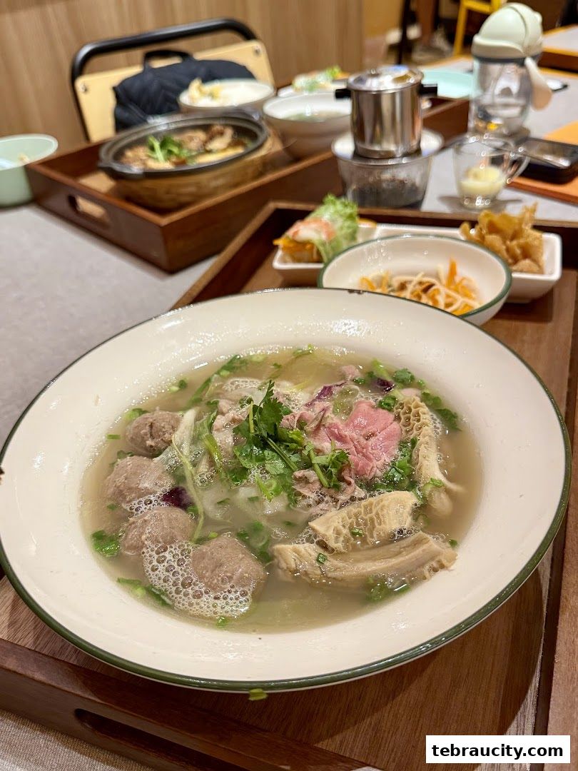 A close-up of a steaming bowl of Vietnamese pho with beef and tripe, served with side dishes.