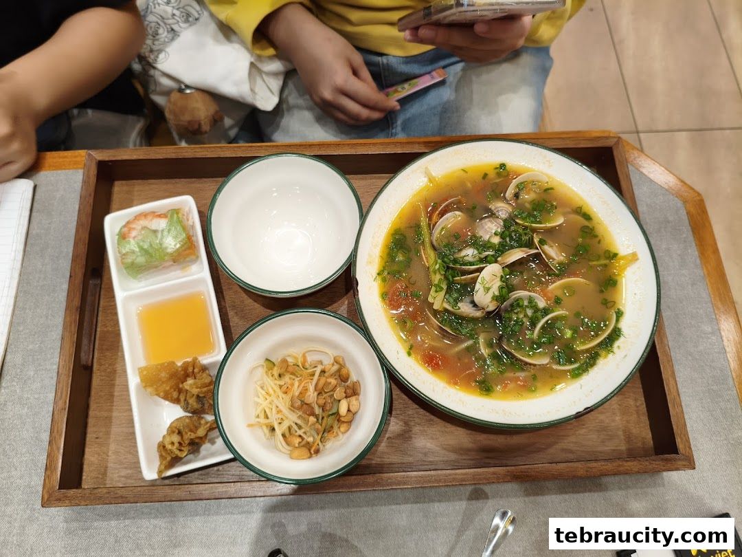 A tray of Vietnamese food featuring a clam soup, spring roll, fried wontons, and papaya salad.