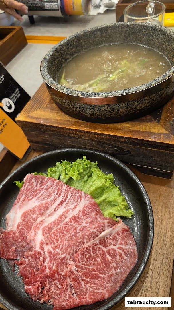 A close-up of thinly sliced raw beef and a bowl of simmering broth with green onions.