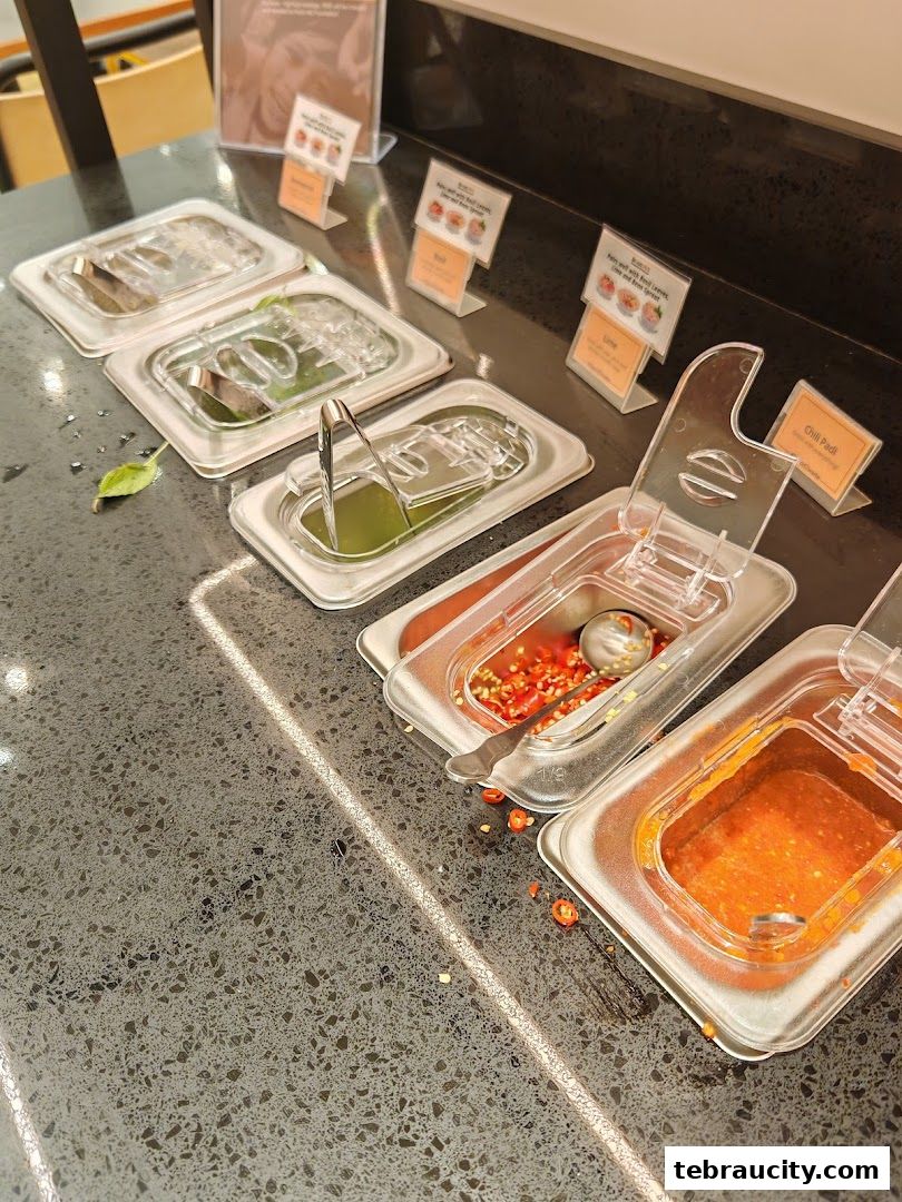 A selection of condiments and fresh ingredients displayed in clear containers on a counter.