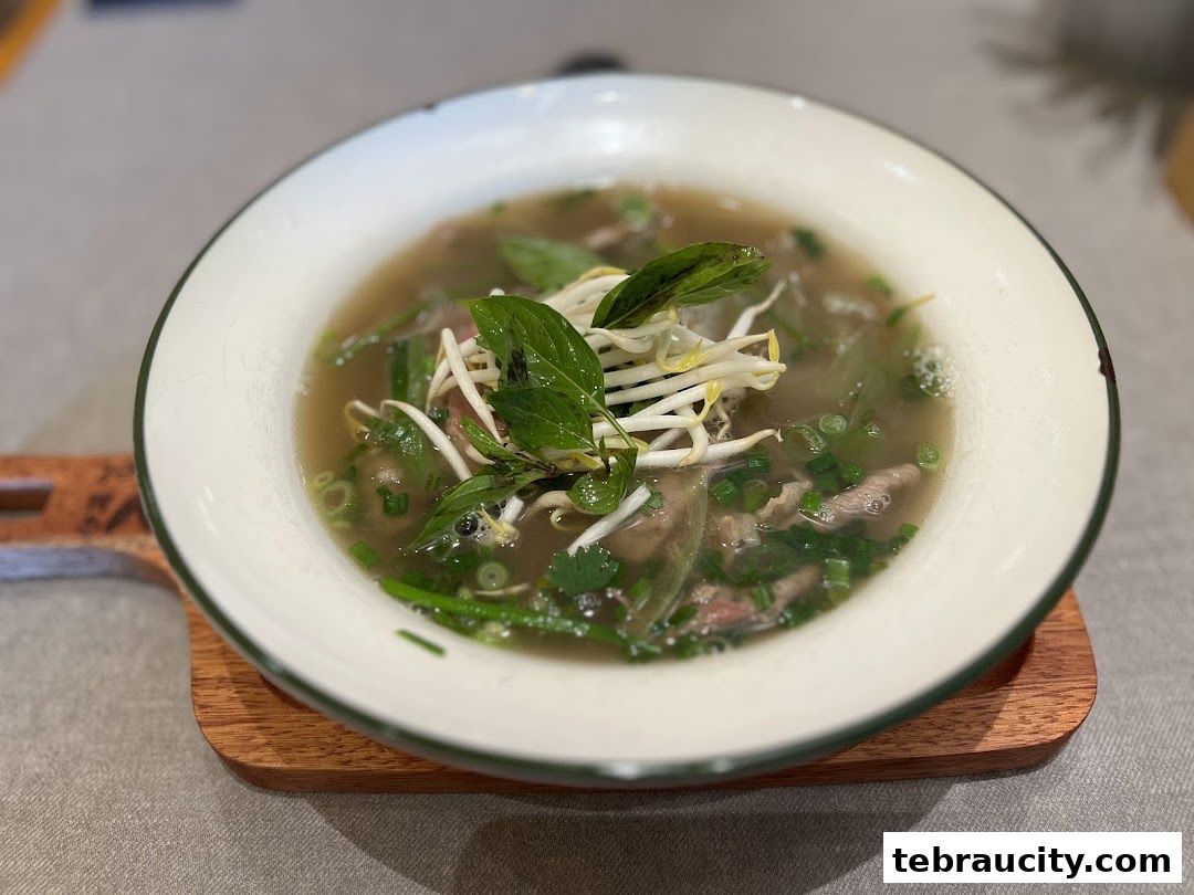 A close-up shot of a steaming bowl of Vietnamese pho with beef, herbs, and bean sprouts.