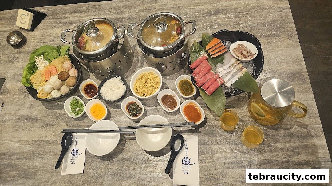 A table set for shabu-shabu with two pots, assorted ingredients, dipping sauces, and drinks.