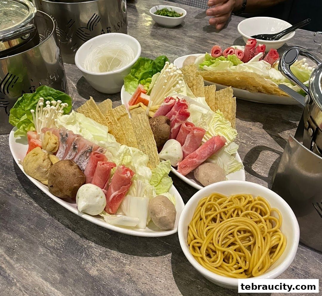 Plates of fresh ingredients for shabu-shabu, including meat, vegetables, and noodles.