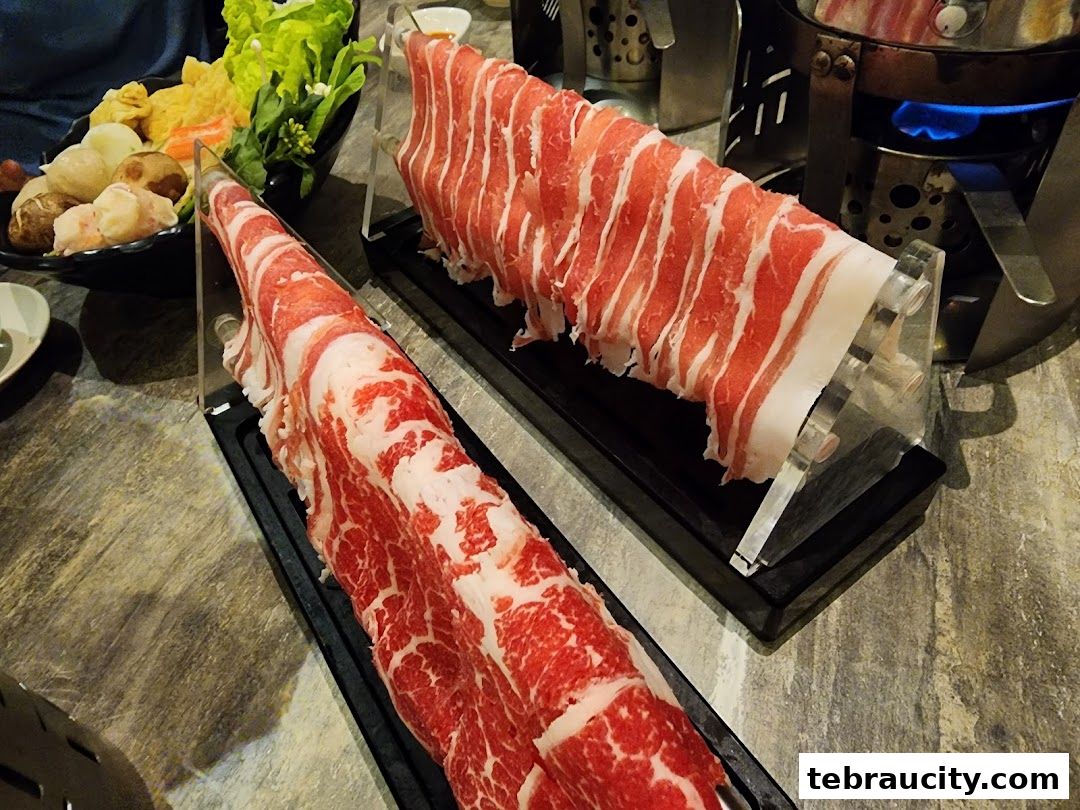 Two platters of thinly sliced raw beef for shabu-shabu, with a pot and vegetables in the background.