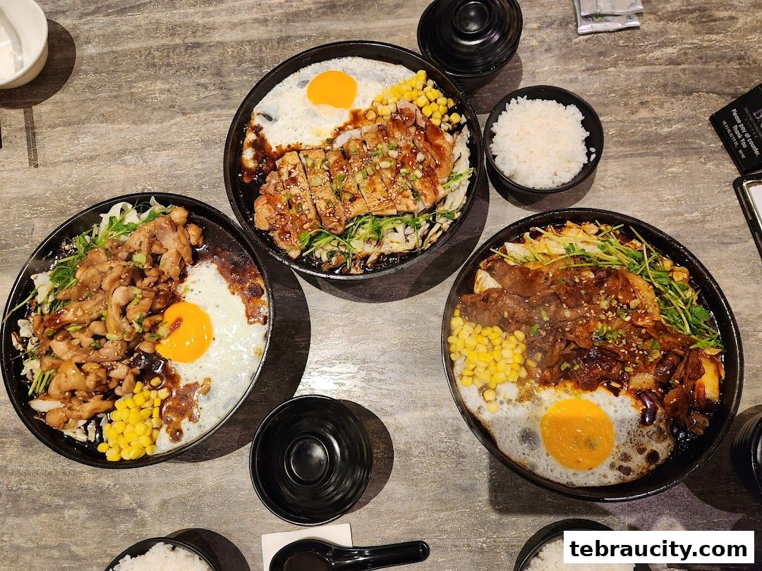 Three sizzling hot plates of Japanese rice bowls with meat, egg, and vegetables.