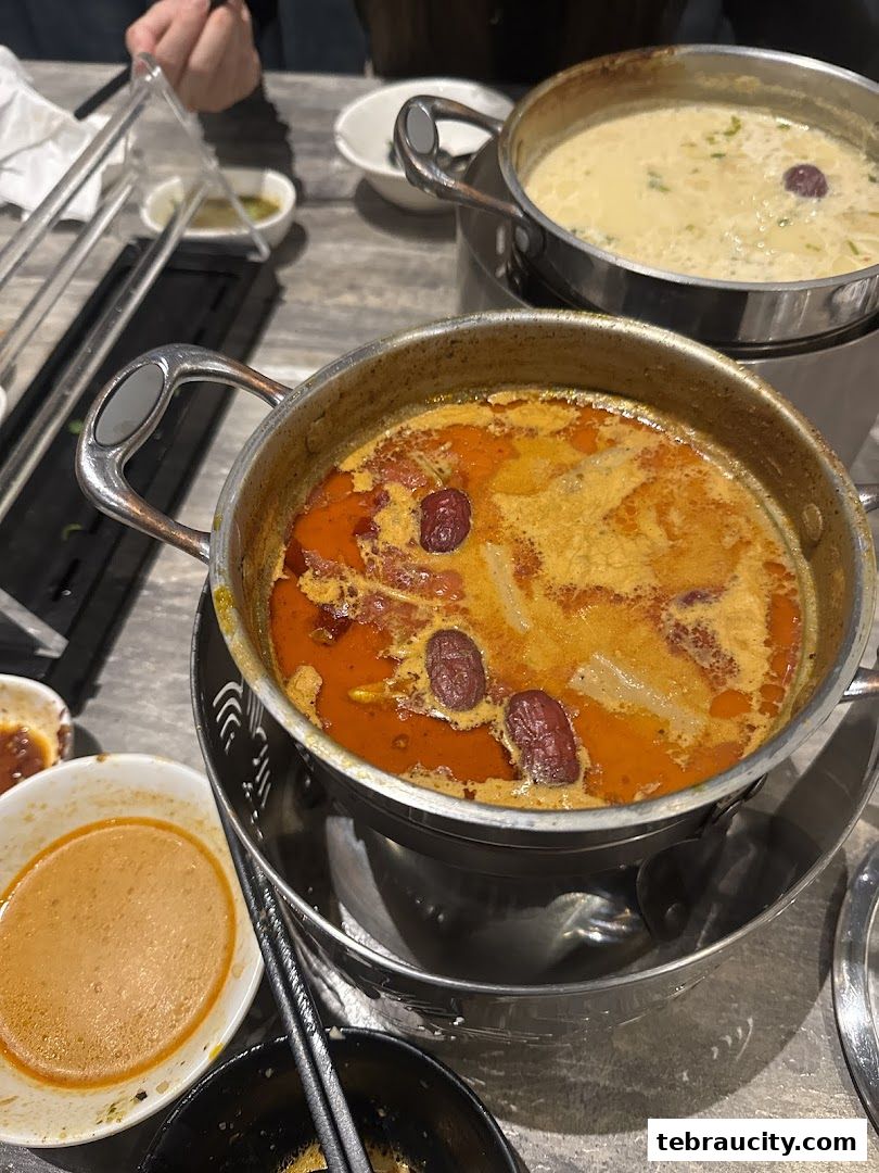 Two pots of shabu-shabu broth, one spicy and one creamy, with ingredients like dates.