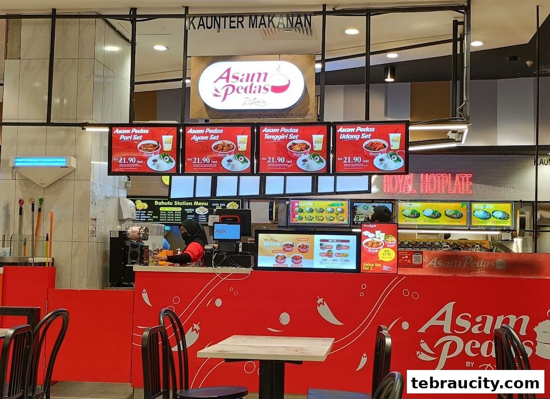 A food counter with digital menus displaying Asam Pedas sets and a vibrant red facade.