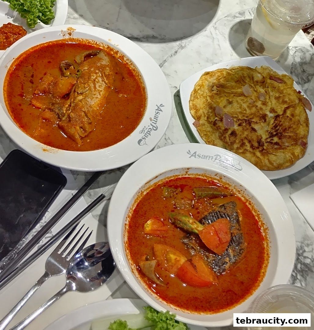 Two bowls of Asam Pedas fish curry with a side of Roti Canai and a drink.