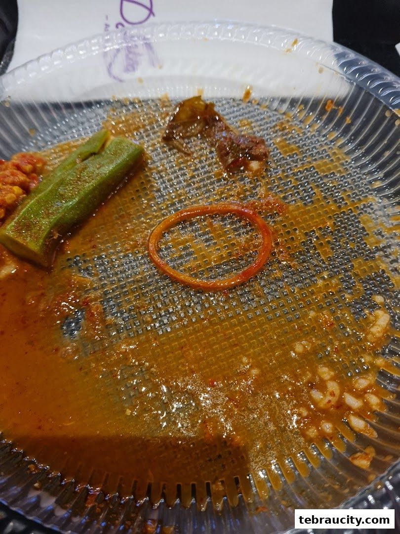 A close-up of a used plastic plate with leftover food and sauce, showing okra and meat remnants.