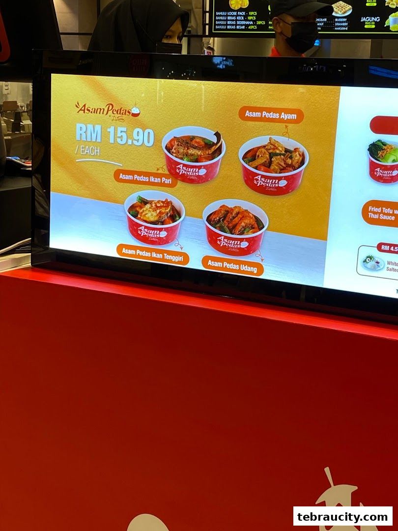 A digital menu board displaying various Asam Pedas dishes with prices.