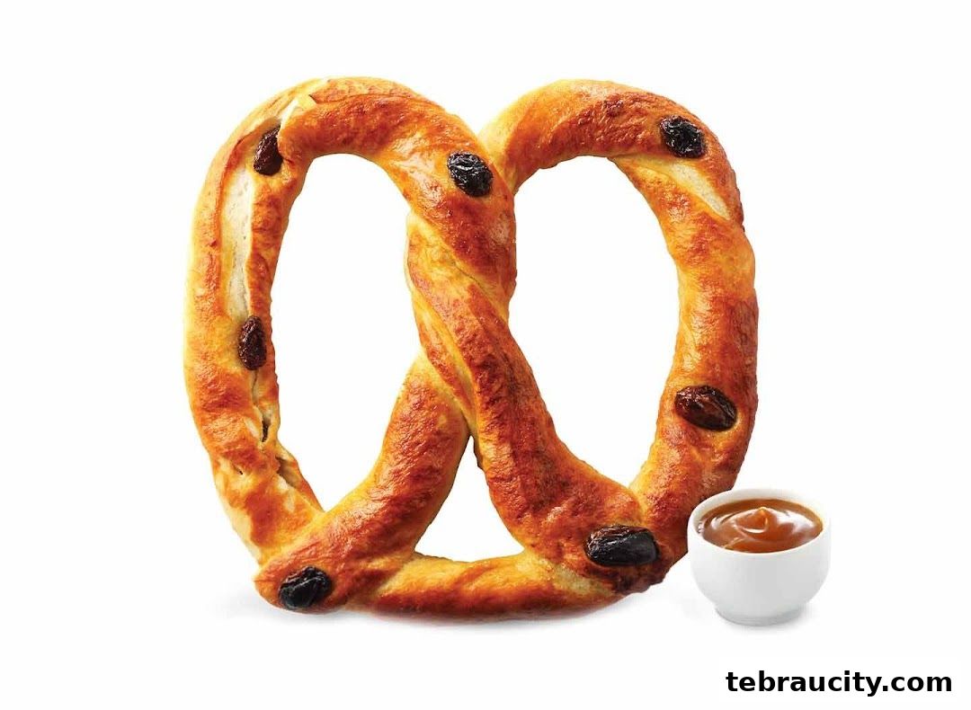 A golden-brown pretzel with raisins and a side of caramel dip.