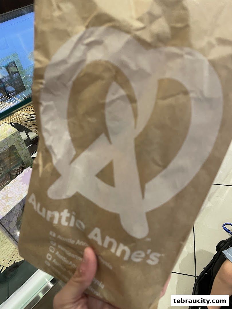 A person holds a brown paper bag with the Auntie Anne's logo.
