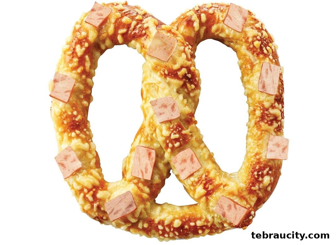 A close-up shot of a golden-brown pretzel topped with melted cheese and square pieces of ham.