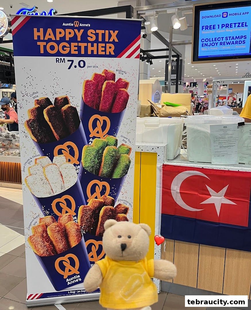 Auntie Anne's promotes their 'Happy Stix Together' pretzel promotion with a large banner and a teddy bear.