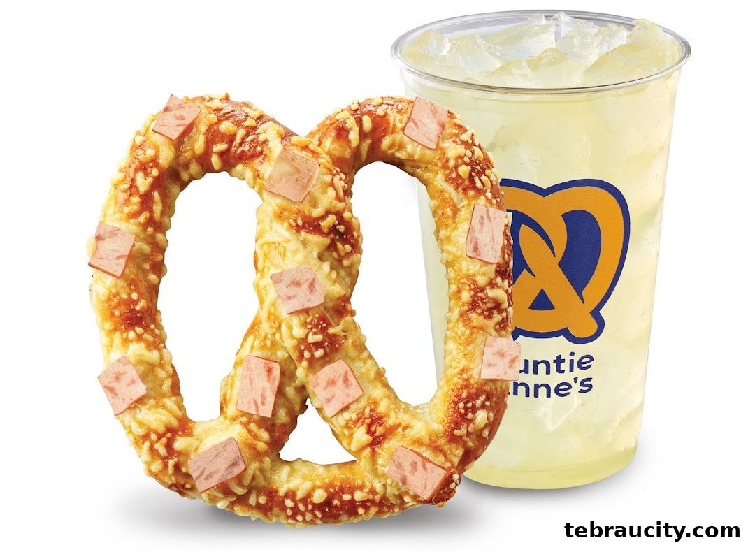 A cheese-covered pretzel with ham pieces next to a lemonade drink with the Auntie Anne's logo.