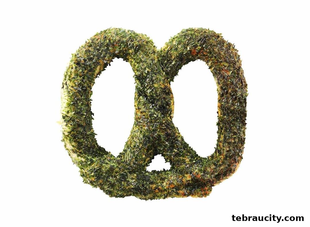 A close-up shot of a pretzel covered in green herbs against a white background.
