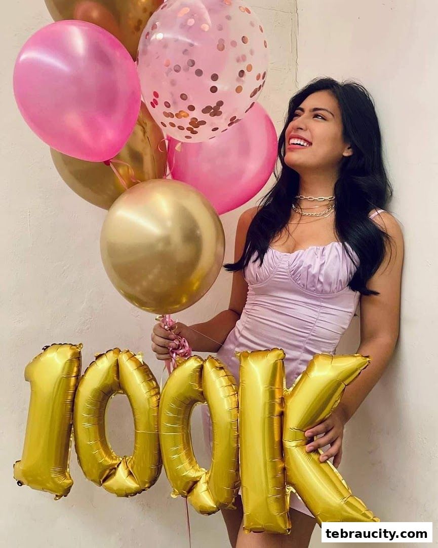 A woman in a purple dress holds balloons and '100K' foil letters.