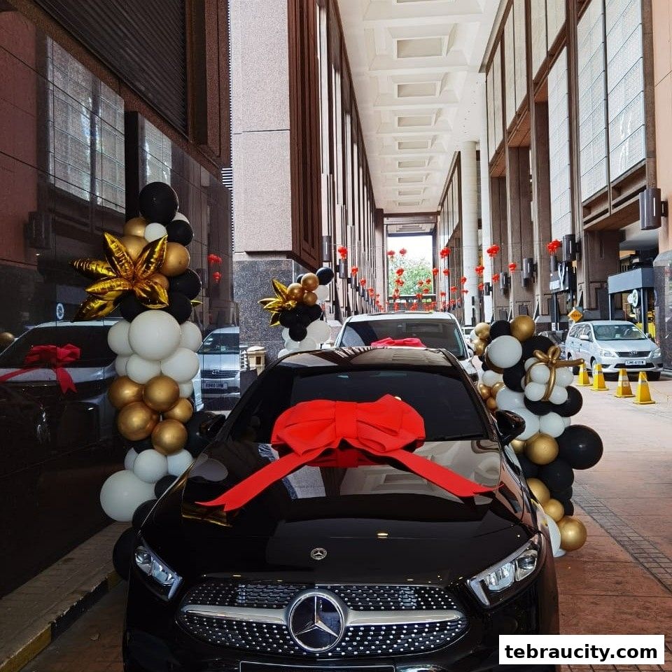A black car decorated with a large red bow and balloon arrangements.