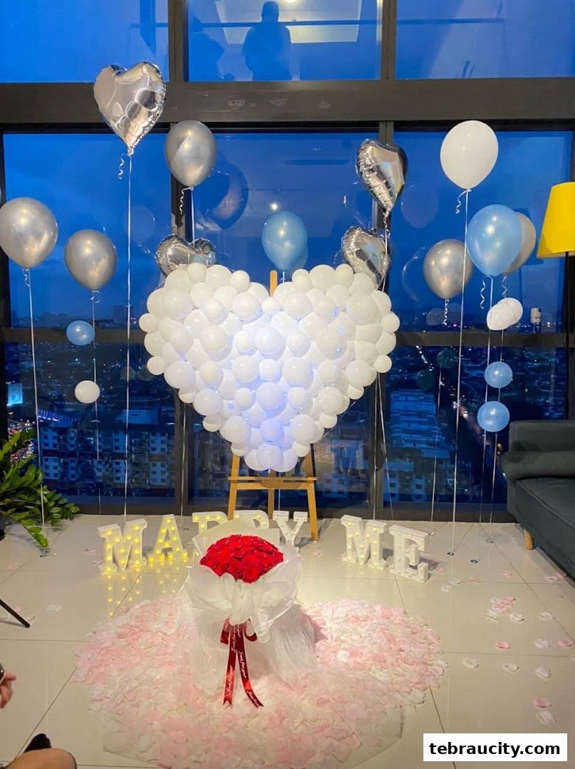 A romantic proposal setup with a heart-shaped balloon arch, roses, and 'Marry Me' lights.