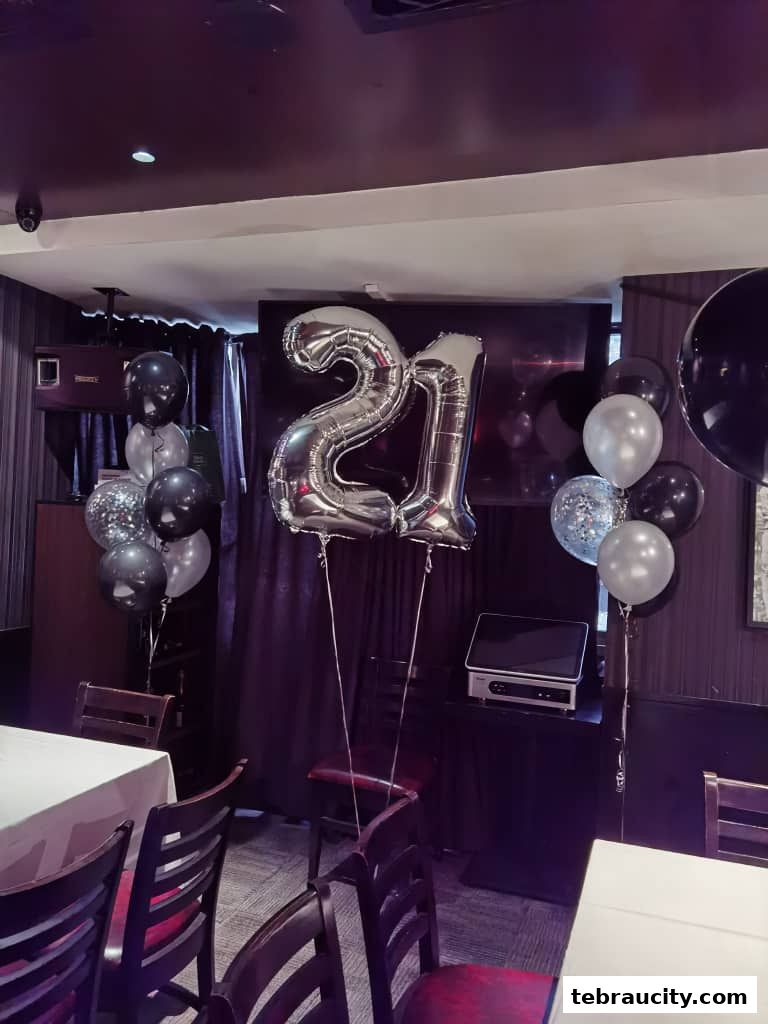 Silver number 21 balloons and black and silver balloons decorate a room with tables and chairs.