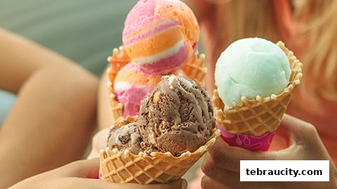 Close-up of hands holding ice cream cones with multiple colorful scoops.