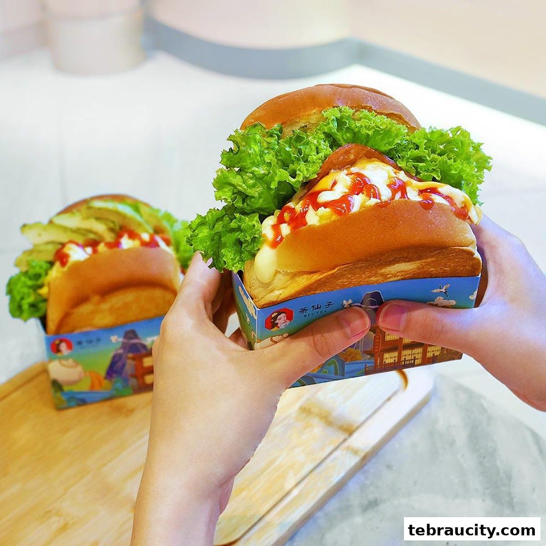 Hands holding delicious-looking burgers with lettuce, cheese, and sauces.