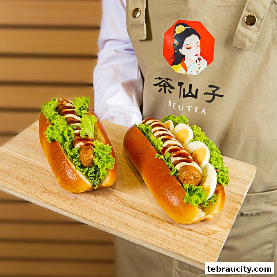 A person holds a wooden board with two delicious hot dogs topped with lettuce, sausage, and sauce.
