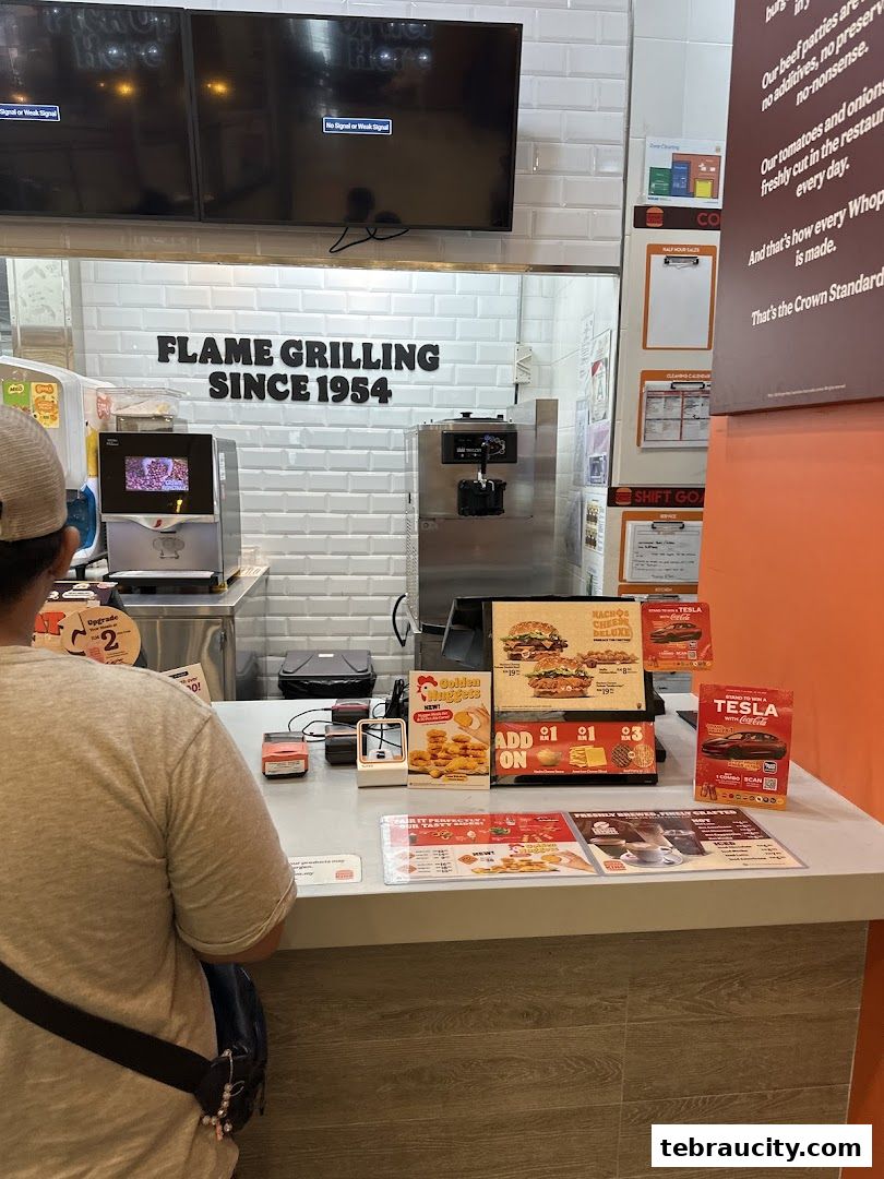 A customer stands at the counter of a Burger King restaurant, with menu displays and promotional materials visible.