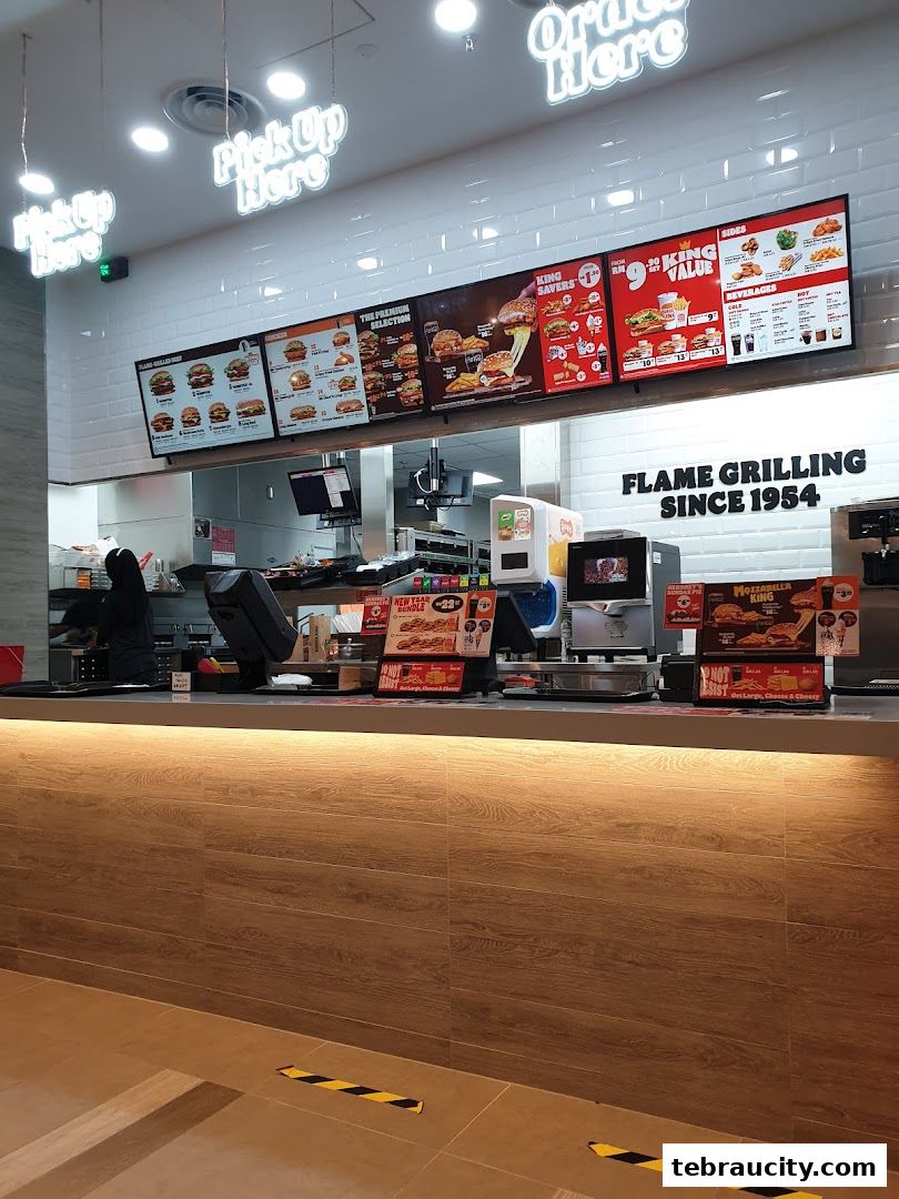 Burger King counter with digital menus displaying burgers and drinks, and 'Pick Up Here' signs.