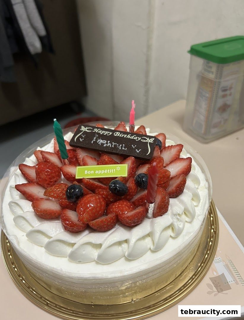 A beautifully decorated birthday cake with strawberries, blueberries, and candles.