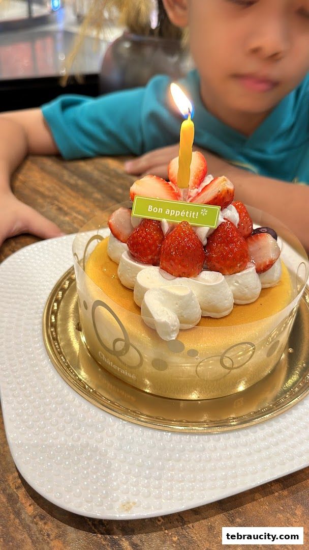 A child looks at a strawberry cake with a lit candle and 'Bon appétit!' sign.
