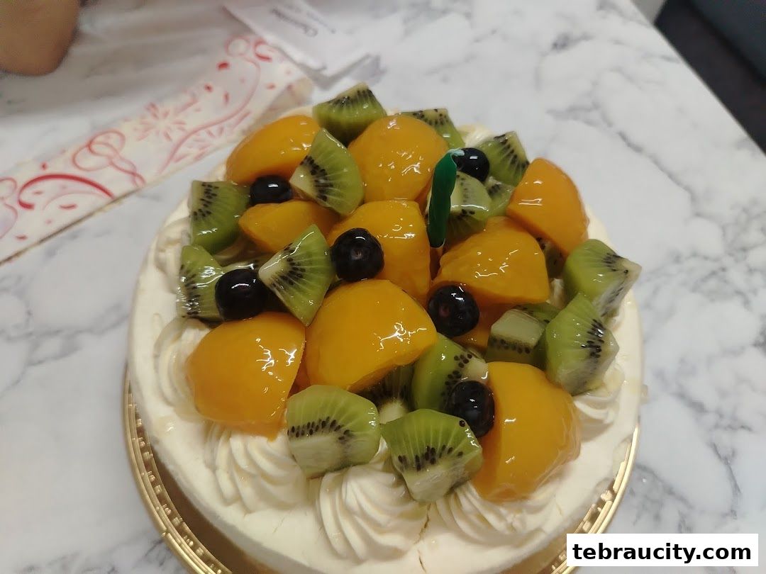A delicious fruit cake topped with kiwi, peaches, and blueberries, ready for celebration.