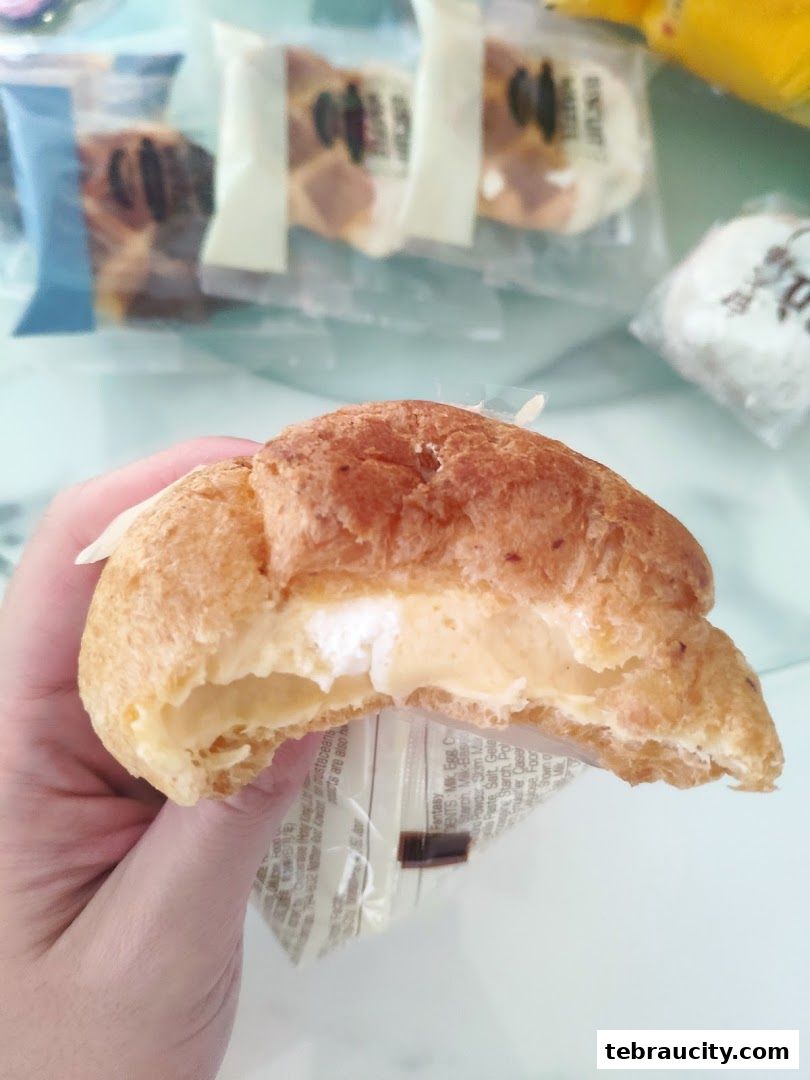 A hand holds a cream puff pastry filled with cream and topped with powdered sugar.
