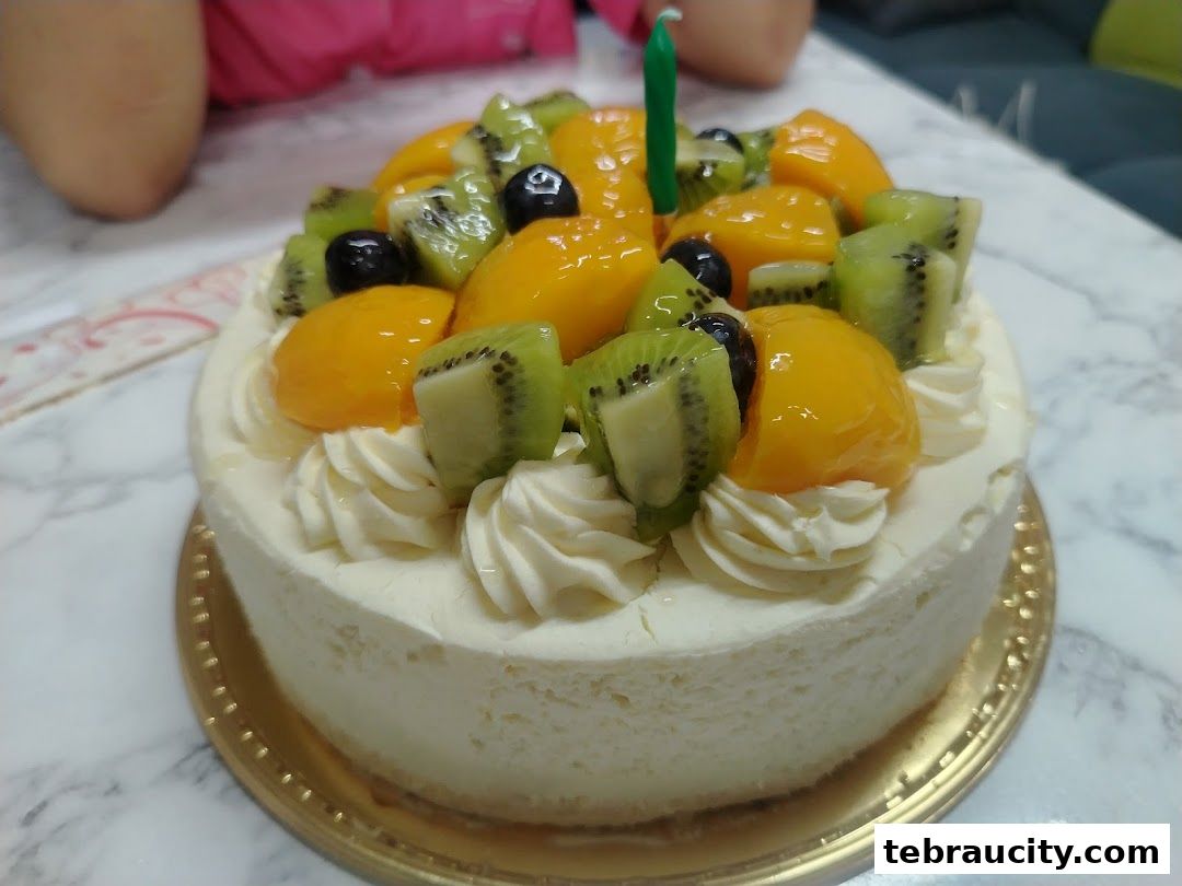 A delicious fruit-topped cake with a single green candle, ready for celebration.